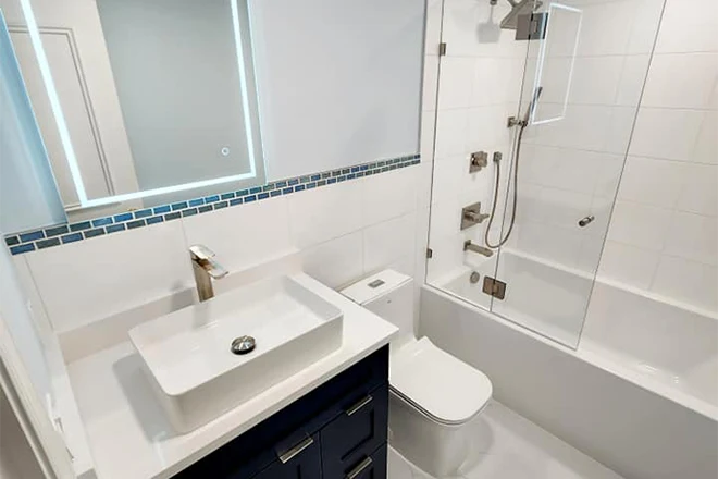 White tile guest bathroom with lit mirror and shower