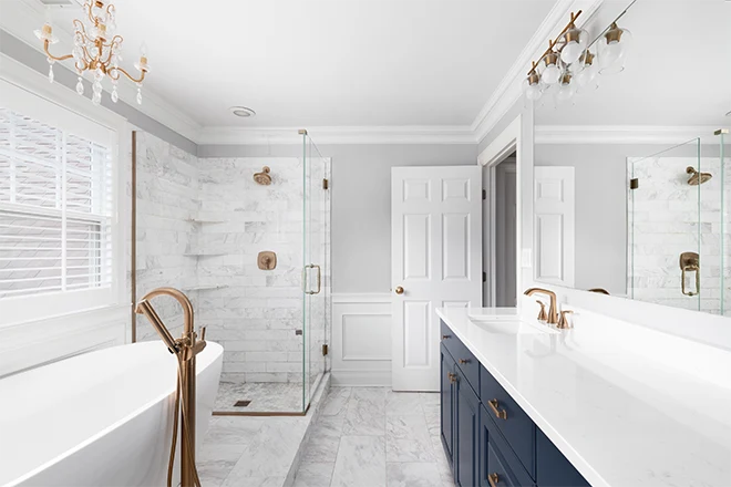 A beautiful bathroom with a blue vanity cabinet standalone bathtub and shower and gold faucets